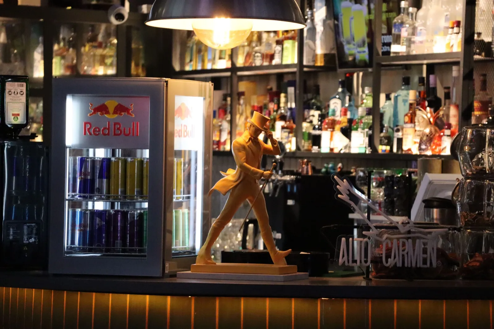 La barra con botellas iluminadas y una figura dorada