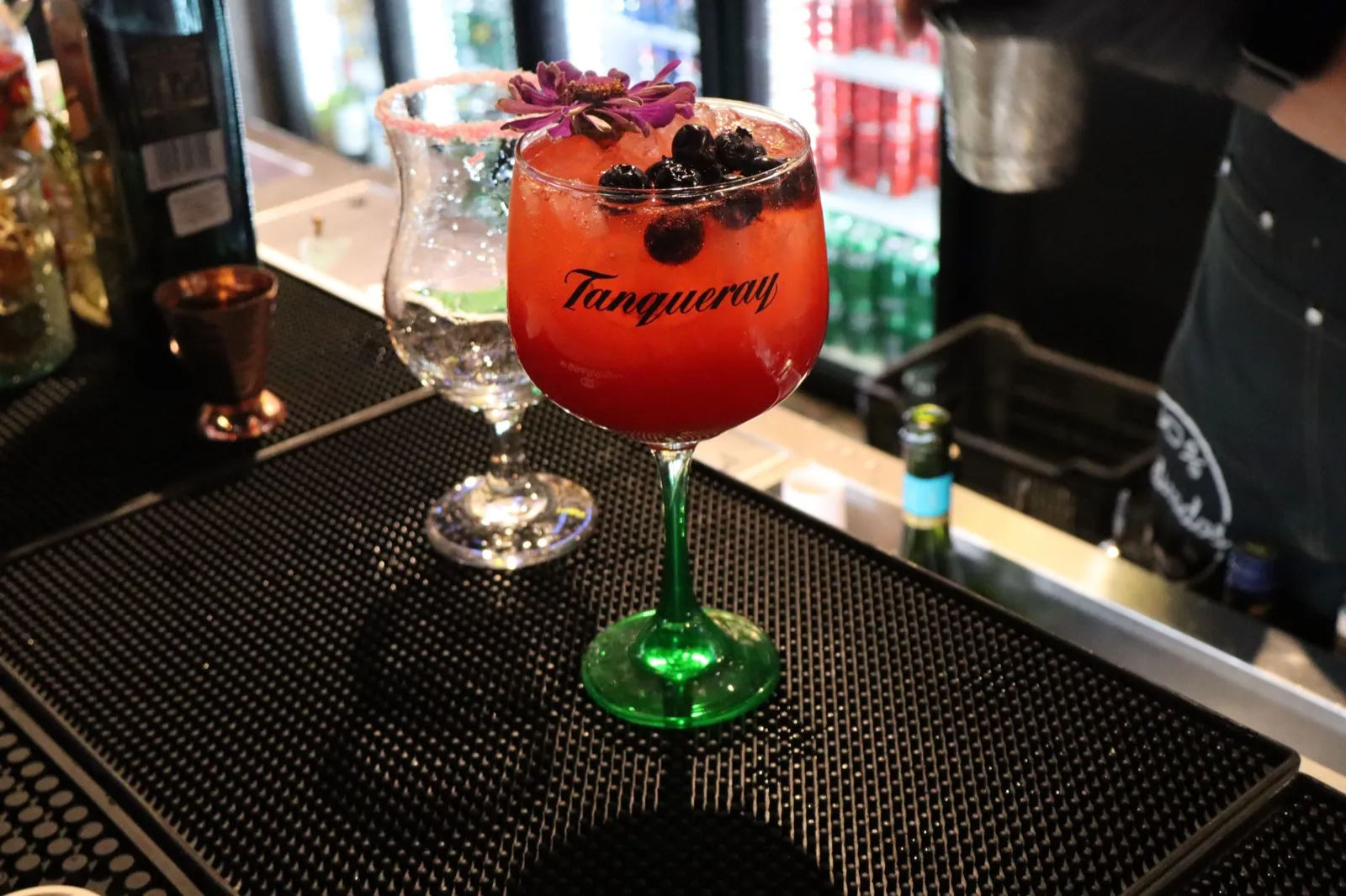 Cóctel rojo con frutos del bosque en copa de tallo verde sobre la barra