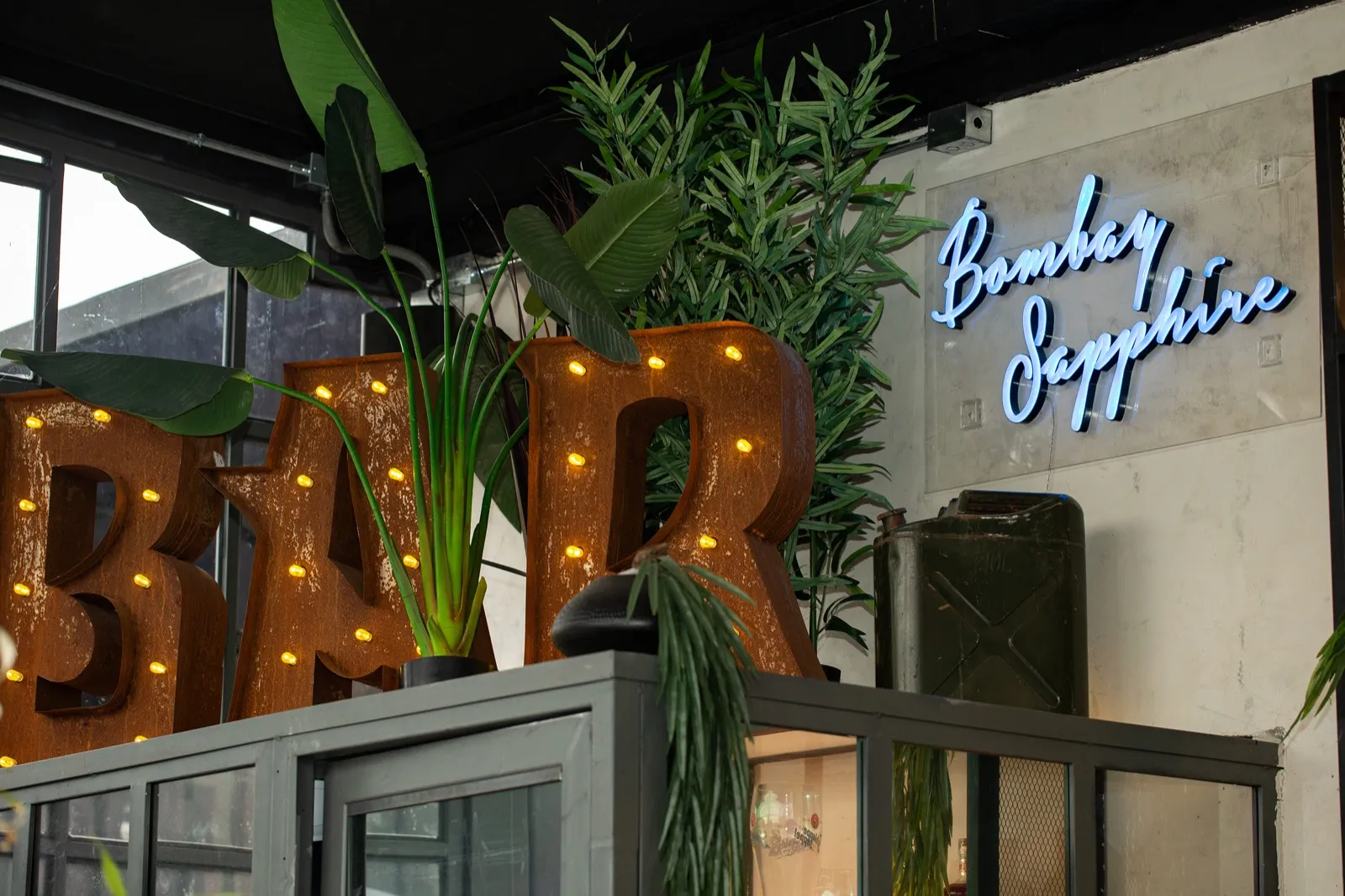 Letrero «BAR» con ampolletas, plantas y un neón en la pared