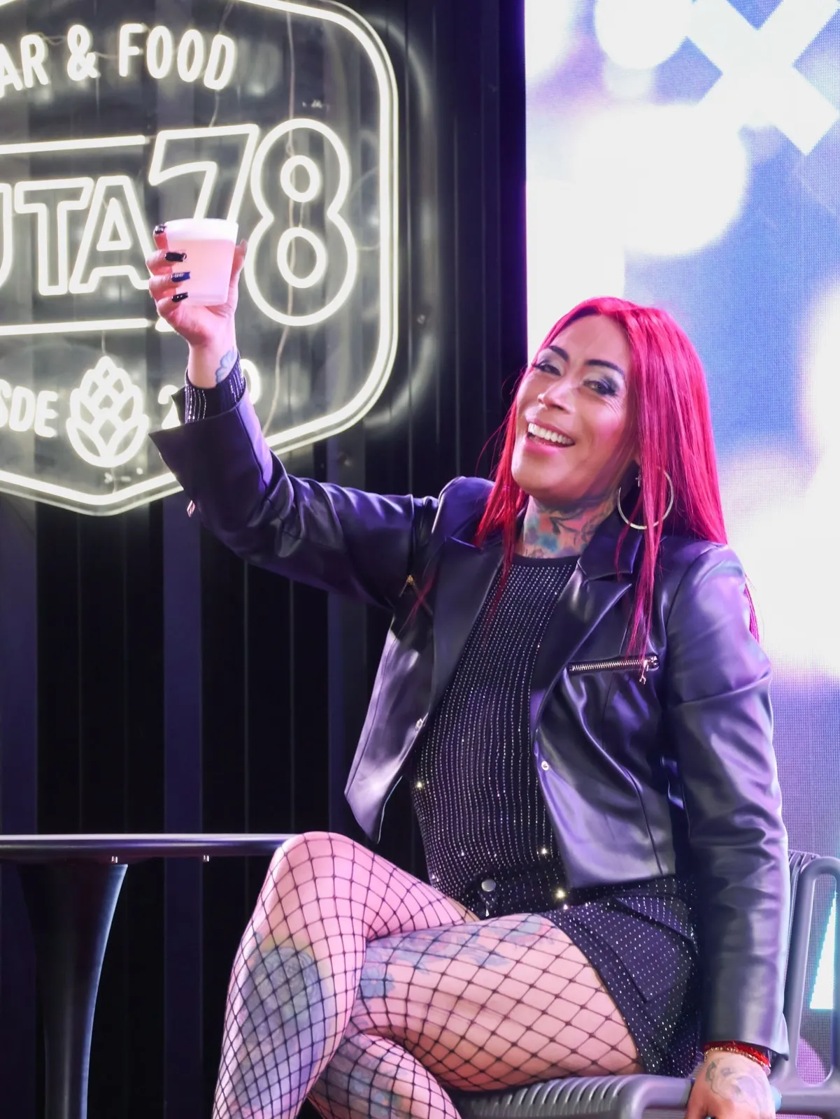Cantante de pelo rojo saludando al público frente al letrero de neón de Ruta 78